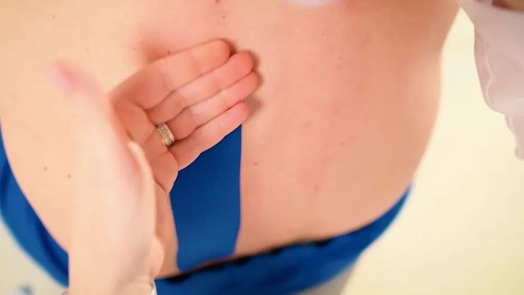 Egy kéz kék kineziológiai tapaszt simít fel egy páciens derekára