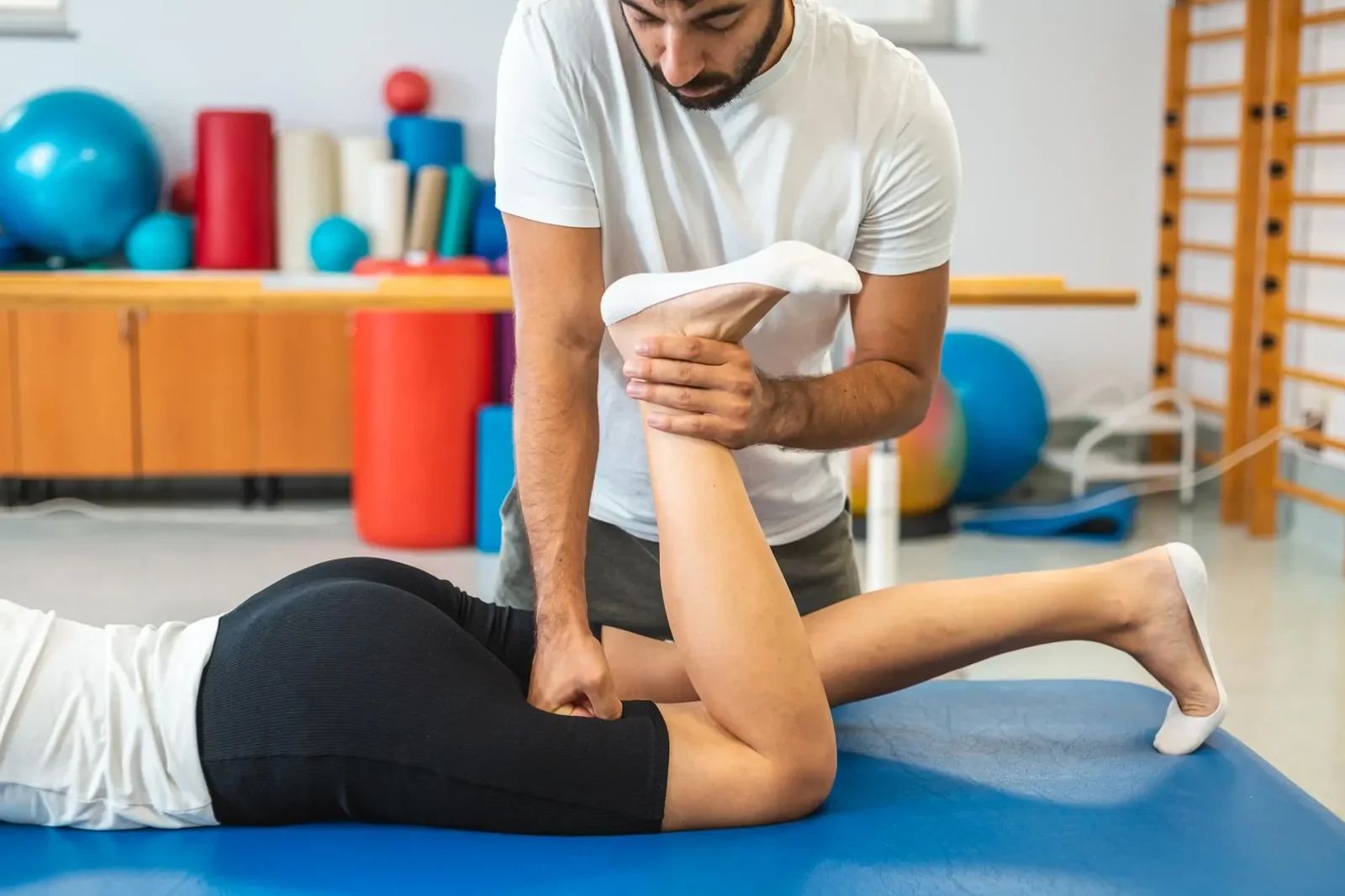 Manuálterápia: a terapeuta a hason fekvő páciens lábát mozgatja át (illusztráció)